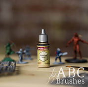 Bottle of the Army Painters Speedpaint in the colour Howling Sand, with wargaming models and an ABC paintbrush in the background, on a wooden surface.