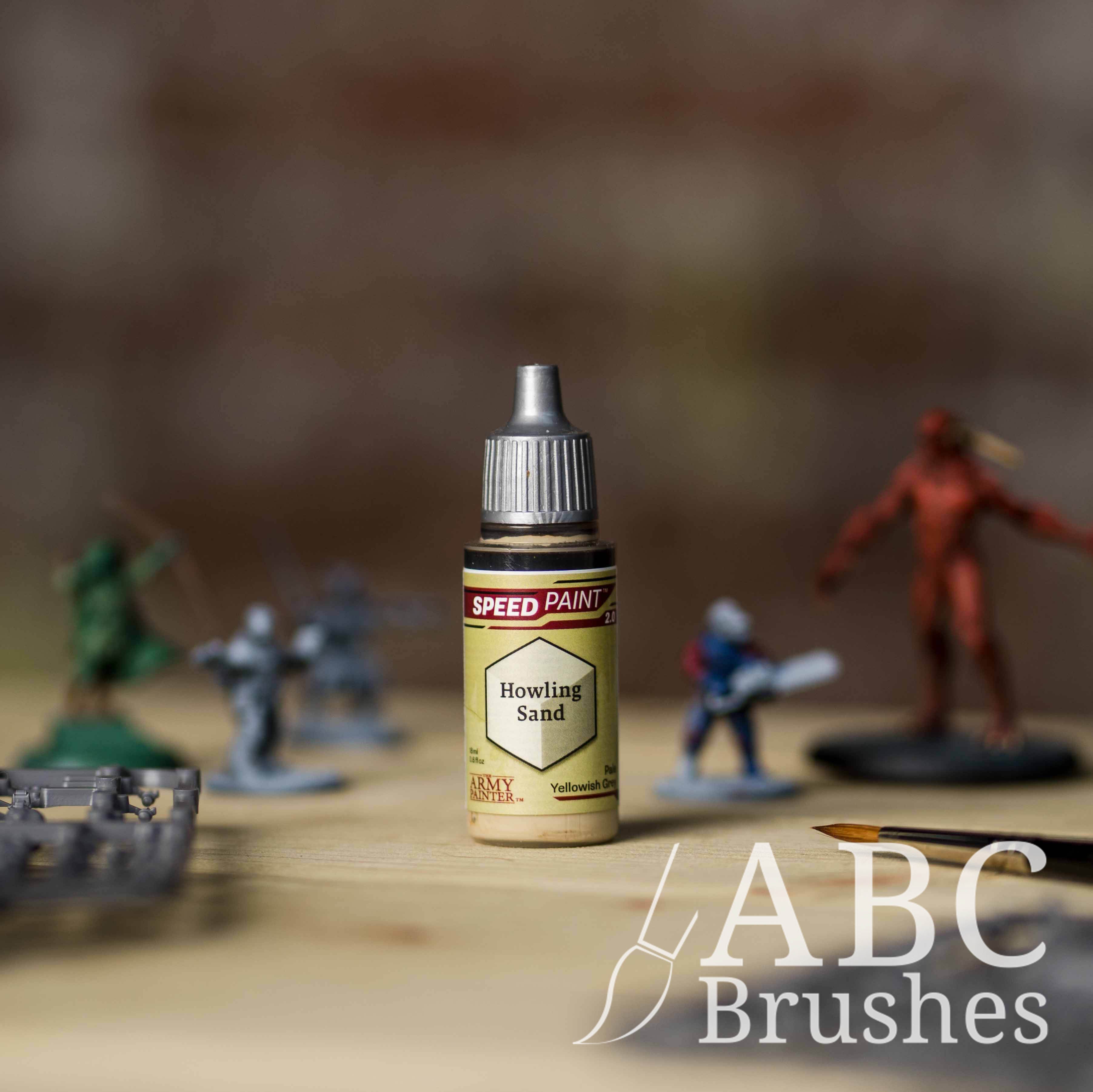Bottle of the Army Painters Speedpaint in the colour Howling Sand, with wargaming models and an ABC paintbrush in the background, on a wooden surface.