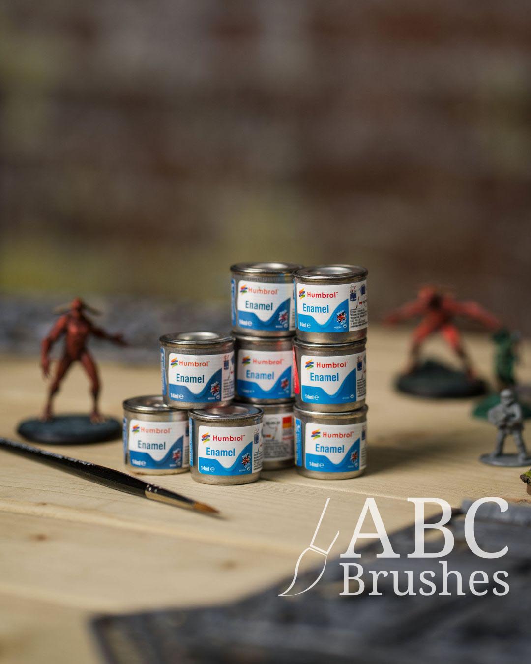 Collection of enamel paint cans on a wooden surface with minis and various miniature painting tools.