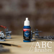 Bottle of the Army Painter Fanatics in the colour Imperial Navy with various wargaming models and an ABC paintbrush in the background, on a wooden surface.