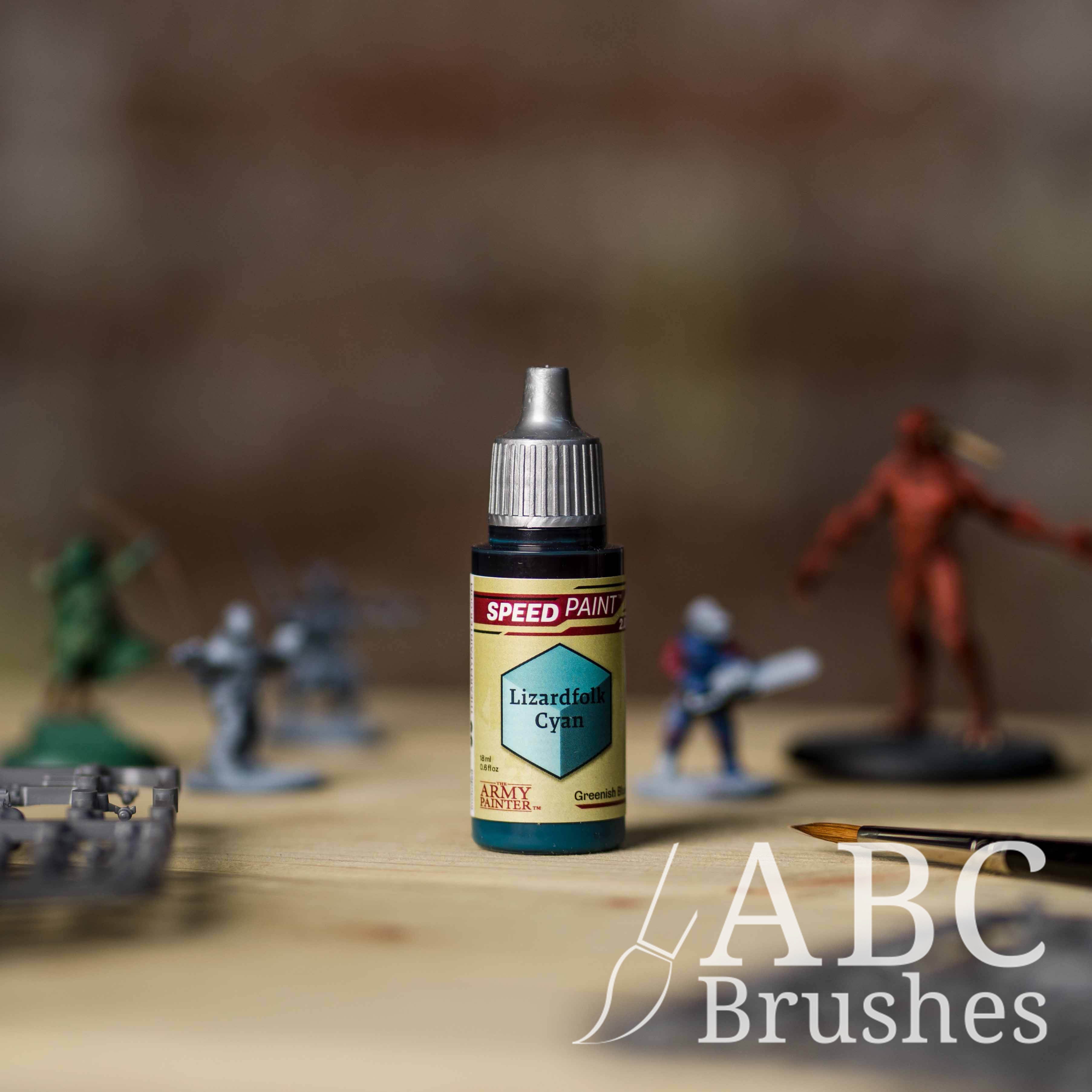 Bottle of the Army Painters Speedpaint in the colour Lizardfolk Cyan, with wargaming models and an ABC paintbrush in the background, on a wooden surface.