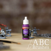 Bottle of the Army Painter Fanatics in the colour Magecast Magenta with various wargaming models and an ABC paintbrush in the background, on a wooden surface.