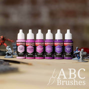 Army Painter Fanatics Magentas Triad on a wooden surface. There are wargaming models and an ABC paint brush next to them.