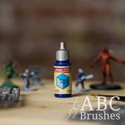 Bottle of the Army Painters Speedpaint in the colour Magic Blue, with wargaming models and an ABC paintbrush in the background, on a wooden surface.