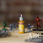 Bottle of the Army Painters Speedpaint in the colour Maize Yellow, with wargaming models and an ABC paintbrush in the background, on a wooden surface.