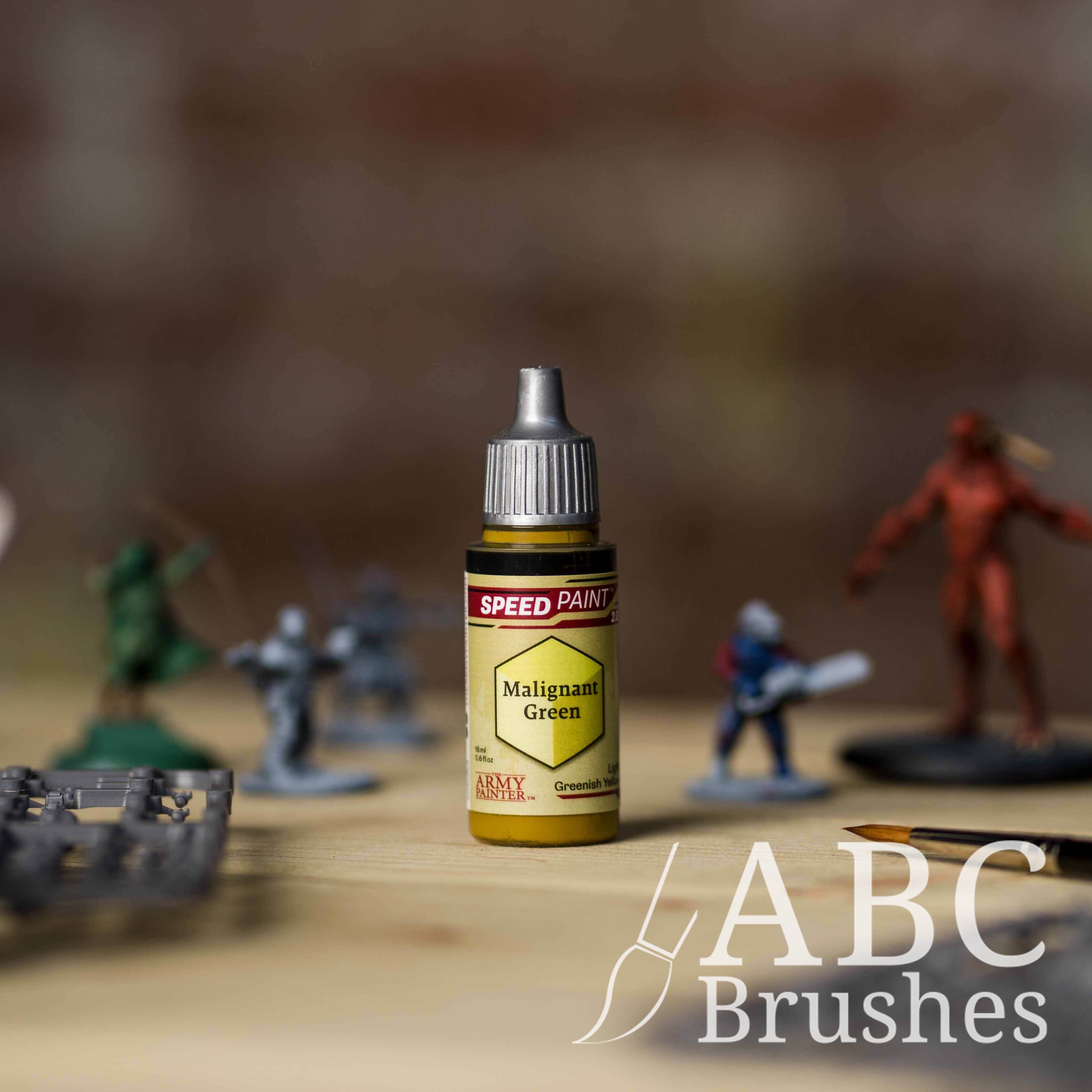 Bottle of the Army Painters Speedpaint in the colour Malignant Green, with wargaming models and an ABC paintbrush in the background, on a wooden surface.