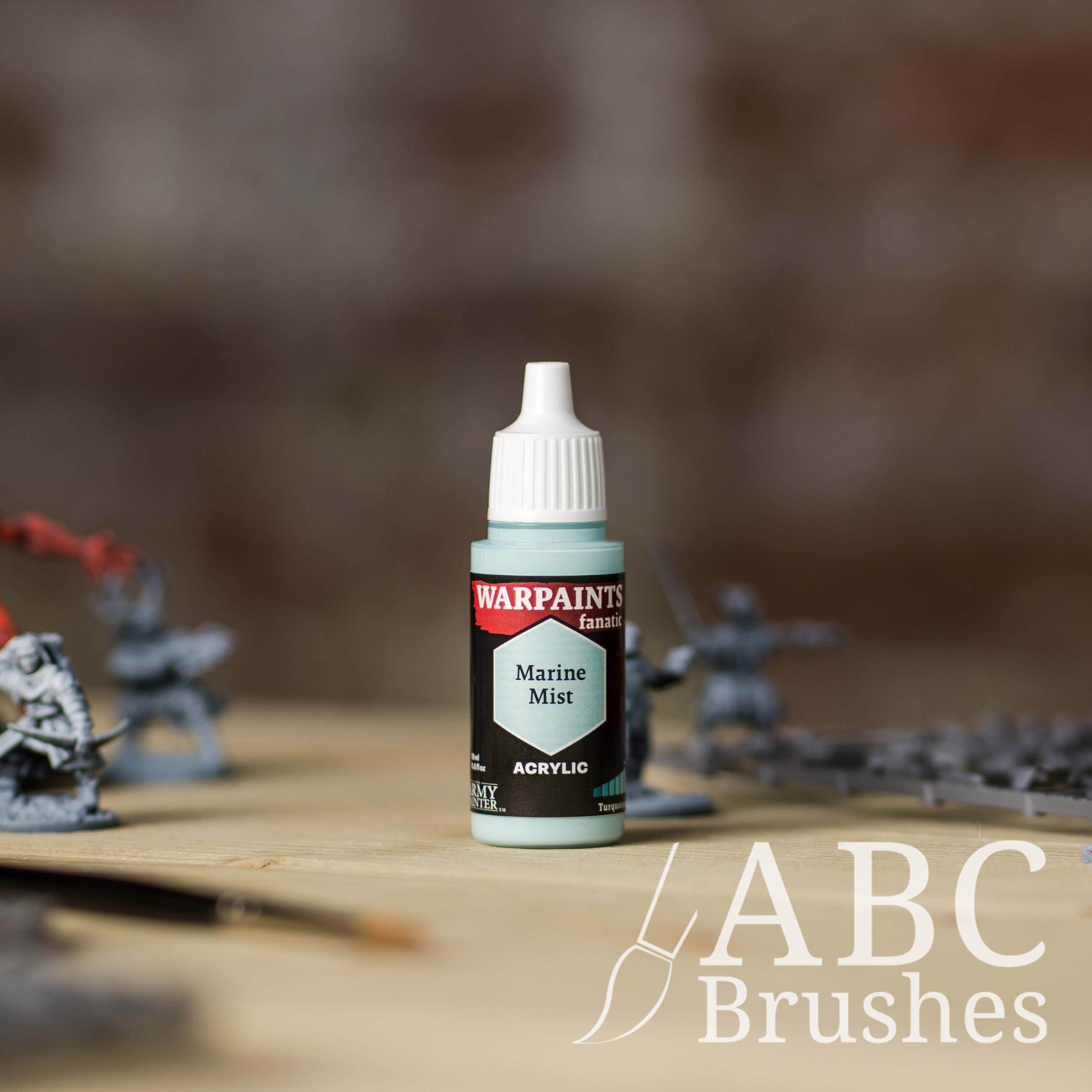 Bottle of the Army Painter Fanatics in the colour Marine Mist with various wargaming models and an ABC paintbrush in the background, on a wooden surface.