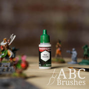 Bottle of the Army Painter Fanatics Effects Matt Varnish with various wargaming models and an ABC paintbrush in the background, on a wooden surface.