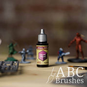 Bottle of the Army Painters Speedpaint in the colour Moody Mauve, with wargaming models and an ABC paintbrush in the background, on a wooden surface.