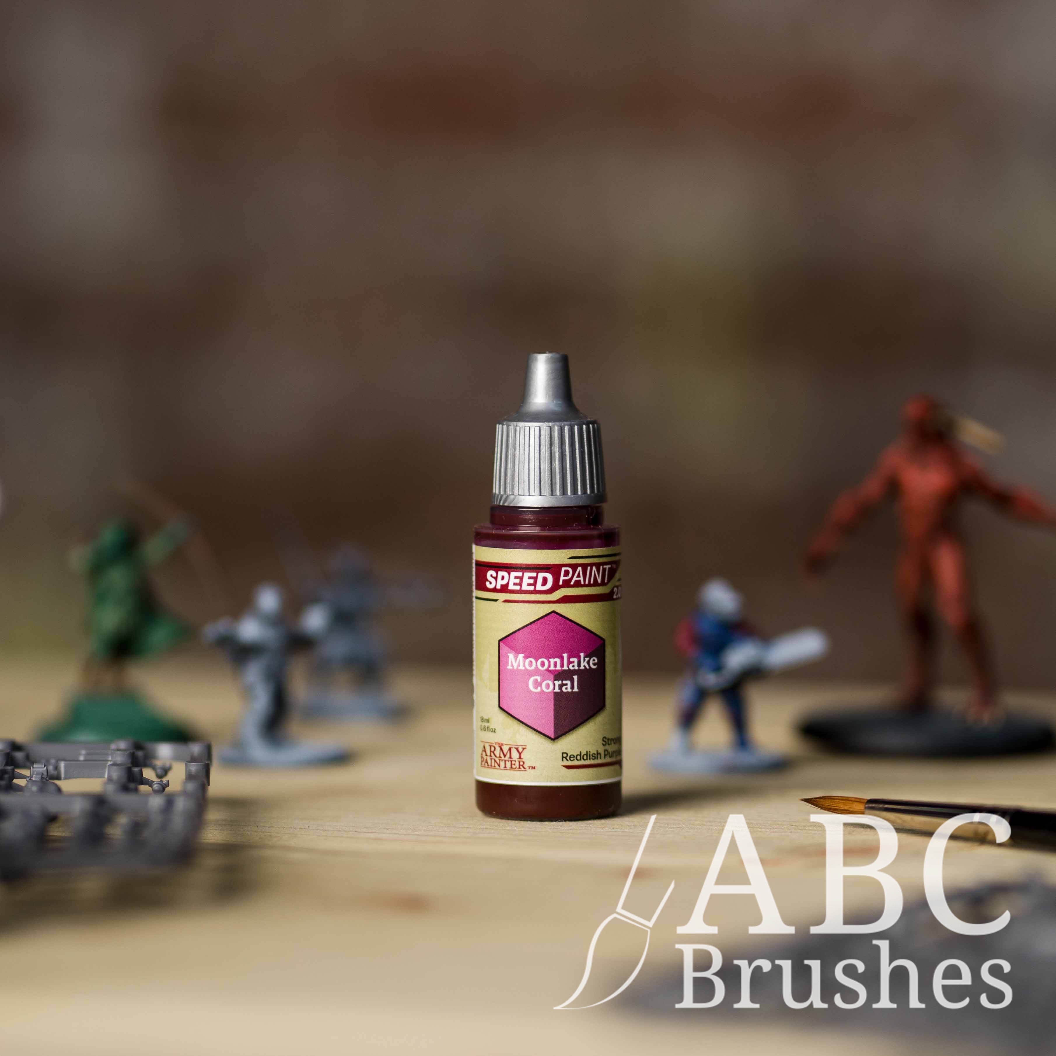 Bottle of the Army Painters Speedpaint in the colour Moonlake Coral, with wargaming models and an ABC paintbrush in the background, on a wooden surface.