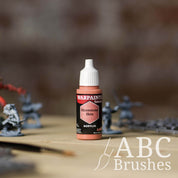 Bottle of the Army Painter Fanatics in the colour Moonstone Skin with various wargaming models and an ABC paintbrush in the background, on a wooden surface.