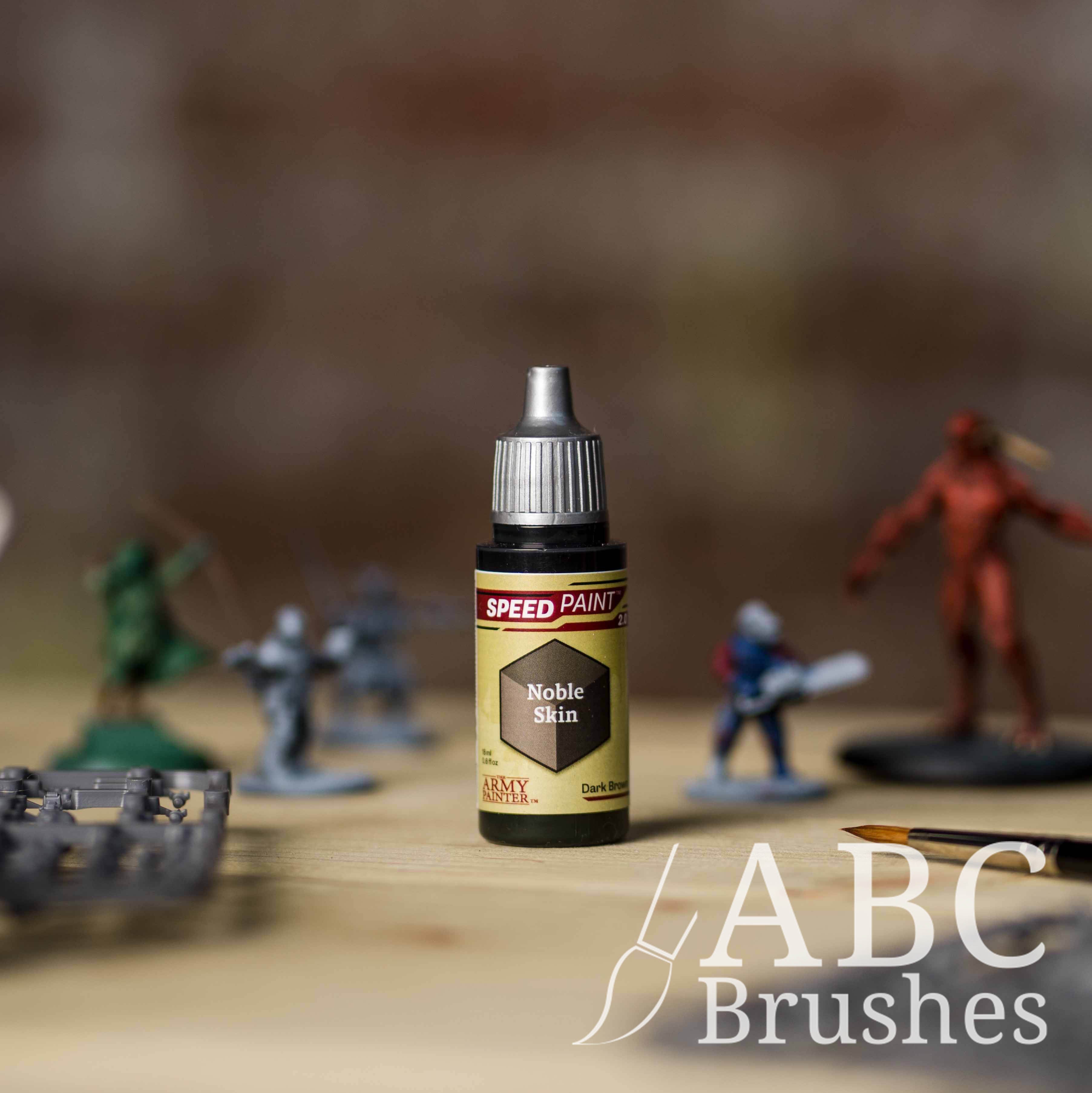Bottle of the Army Painters Speedpaint in the colour Noble Skin, with wargaming models and an ABC paintbrush in the background, on a wooden surface.