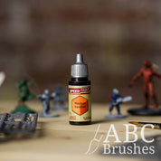 Bottle of the Army Painters Speedpaint in the colour Nuclear Sunrise, with wargaming models and an ABC paintbrush in the background, on a wooden surface.
