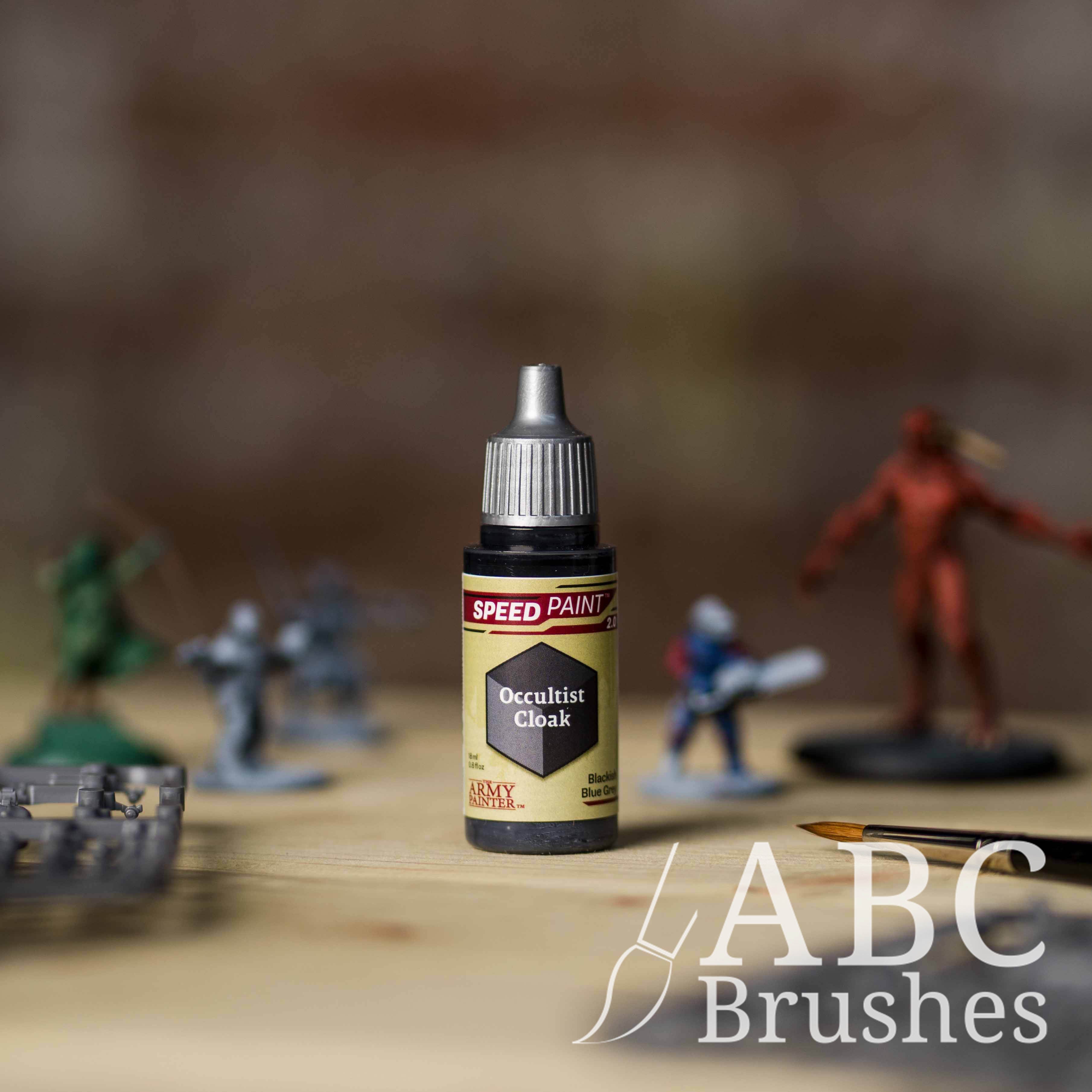 Bottle of the Army Painters Speedpaint in the colour Occultist Cloak, with wargaming models and an ABC paintbrush in the background, on a wooden surface.