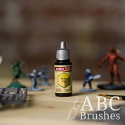 Bottle of the Army Painters Speedpaint in the colour Ochre Clay, with wargaming models and an ABC paintbrush in the background, on a wooden surface.