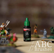 Bottle of the Army Painter Fanatics Effects in the colour Oil Stains with various wargaming models and an ABC paintbrush in the background, on a wooden surface.