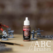 Bottle of the Army Painter Fanatics in the colour Onyx Skin with various wargaming models and an ABC paintbrush in the background, on a wooden surface.