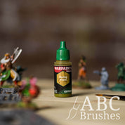 Bottle of the Army Painter Fanatics Effects in the colour Oozing Vomit with various wargaming models and an ABC paintbrush in the background, on a wooden surface.