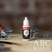 Bottle of the Army Painter Fanatics in the colour Opal Skin with various wargaming models and an ABC paintbrush in the background, on a wooden surface.