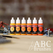 Army Painter Fanatics Oranges Triad on a wooden surface. There are wargaming models and an ABC paint brush next to them.