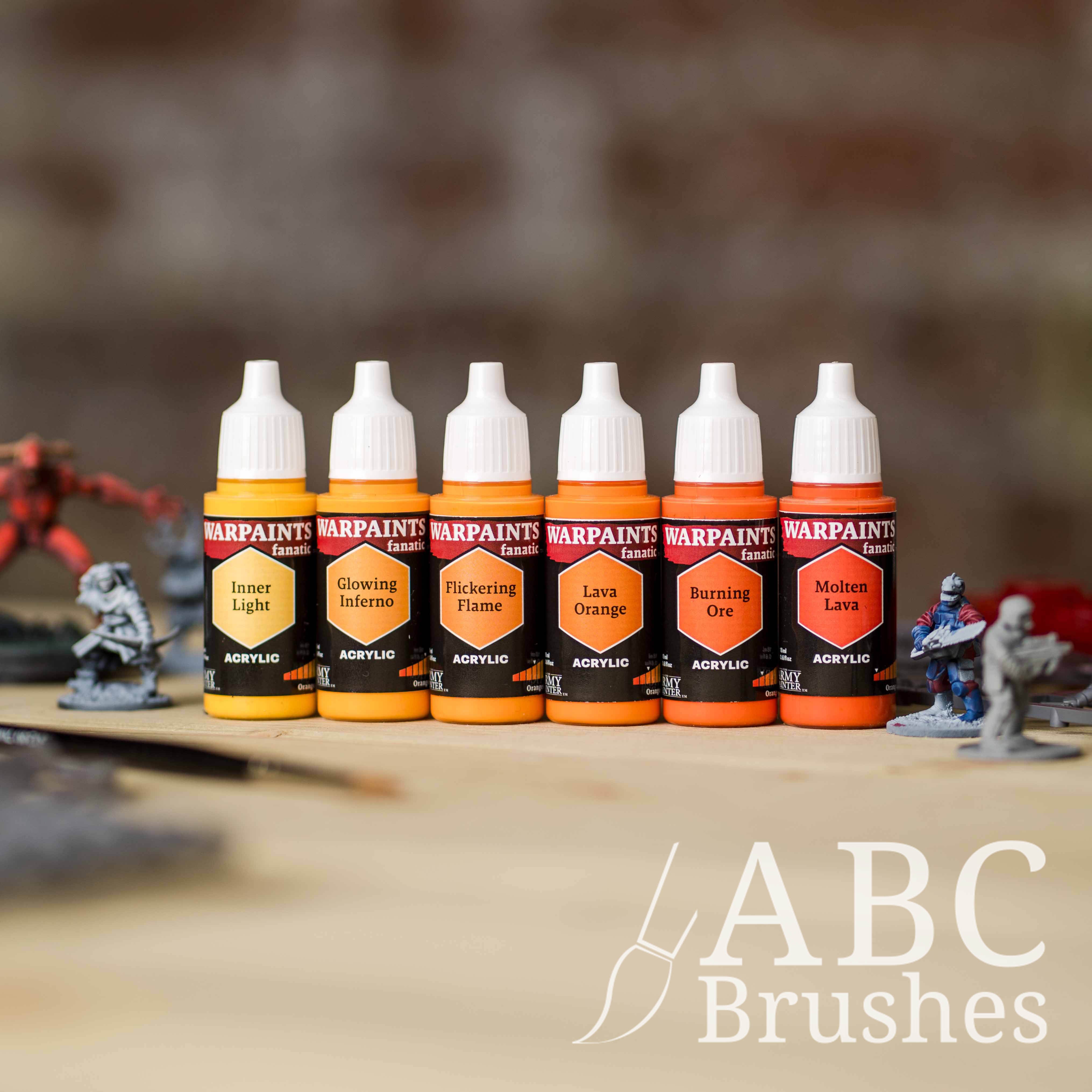 Army Painter Fanatics Oranges Triad on a wooden surface. There are wargaming models and an ABC paint brush next to them.