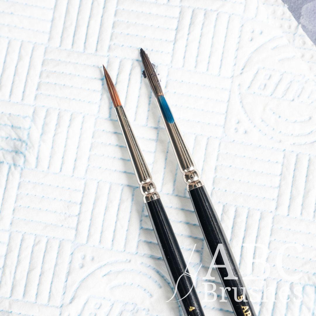 Two paintbrushes, one unused and the other covered in paint placed on top of a paper towel. 
