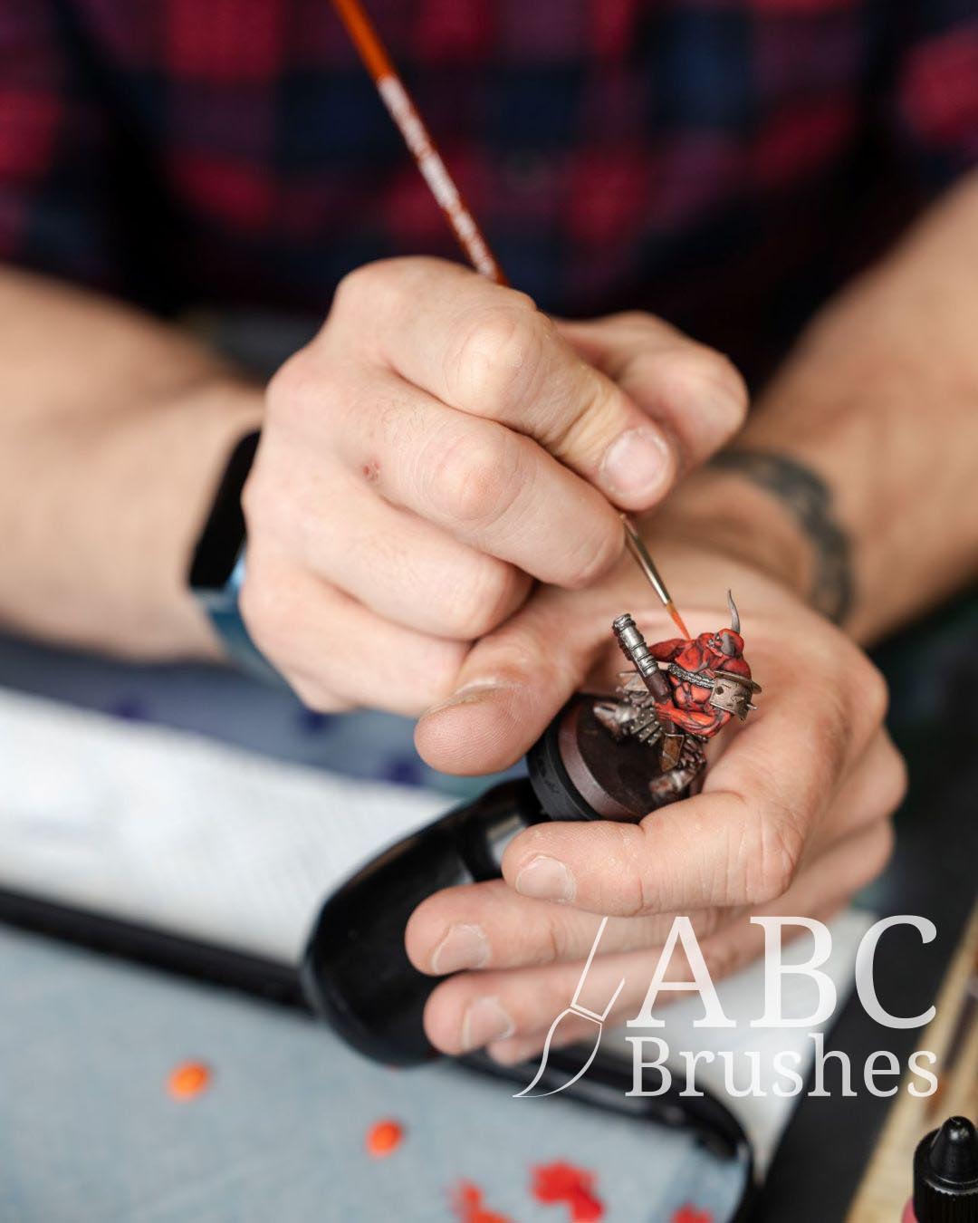 Painting a red demon-like mini with an ABC Sentinel paintbrush.