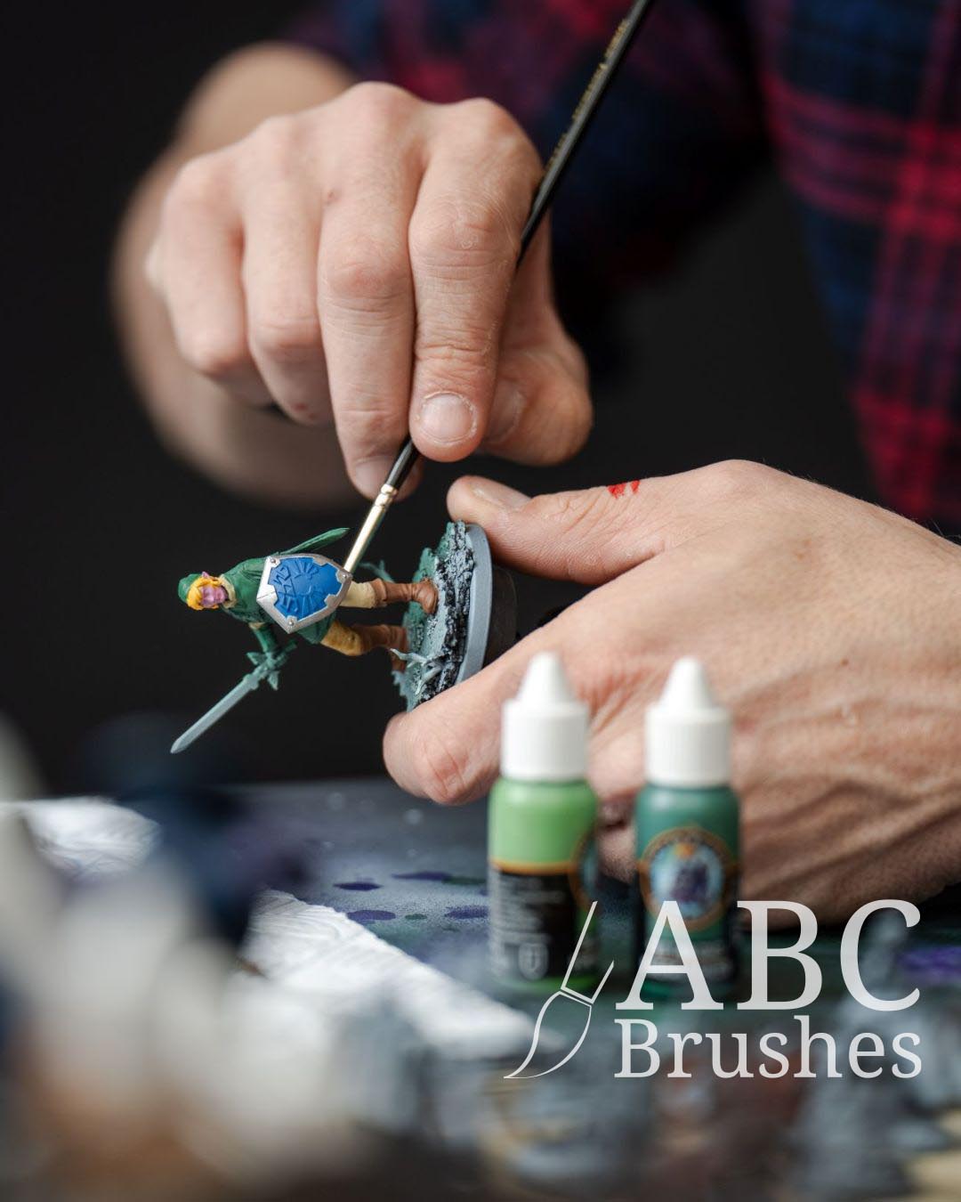 Painting a Legend of Zelda mini figure with an ABC paintbrush and with paint bottles in the foreground.