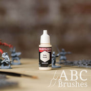 Bottle of the Army Painter Fanatics in the colour Pale Sand with various wargaming models and an ABC paintbrush in the background, on a wooden surface.