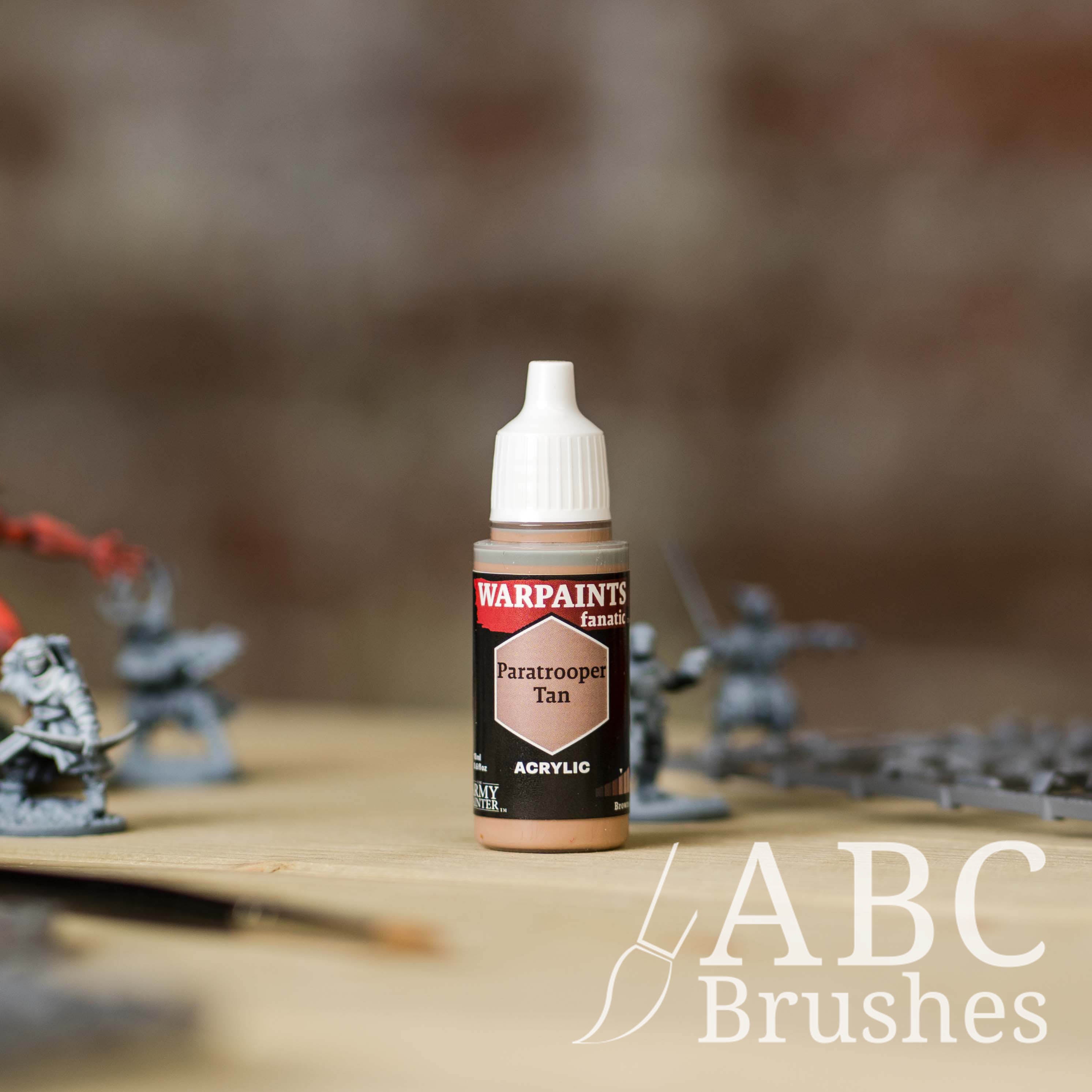 Bottle of the Army Painter Fanatics in the colour Paratrooper Tan with various wargaming models and an ABC paintbrush in the background, on a wooden surface.