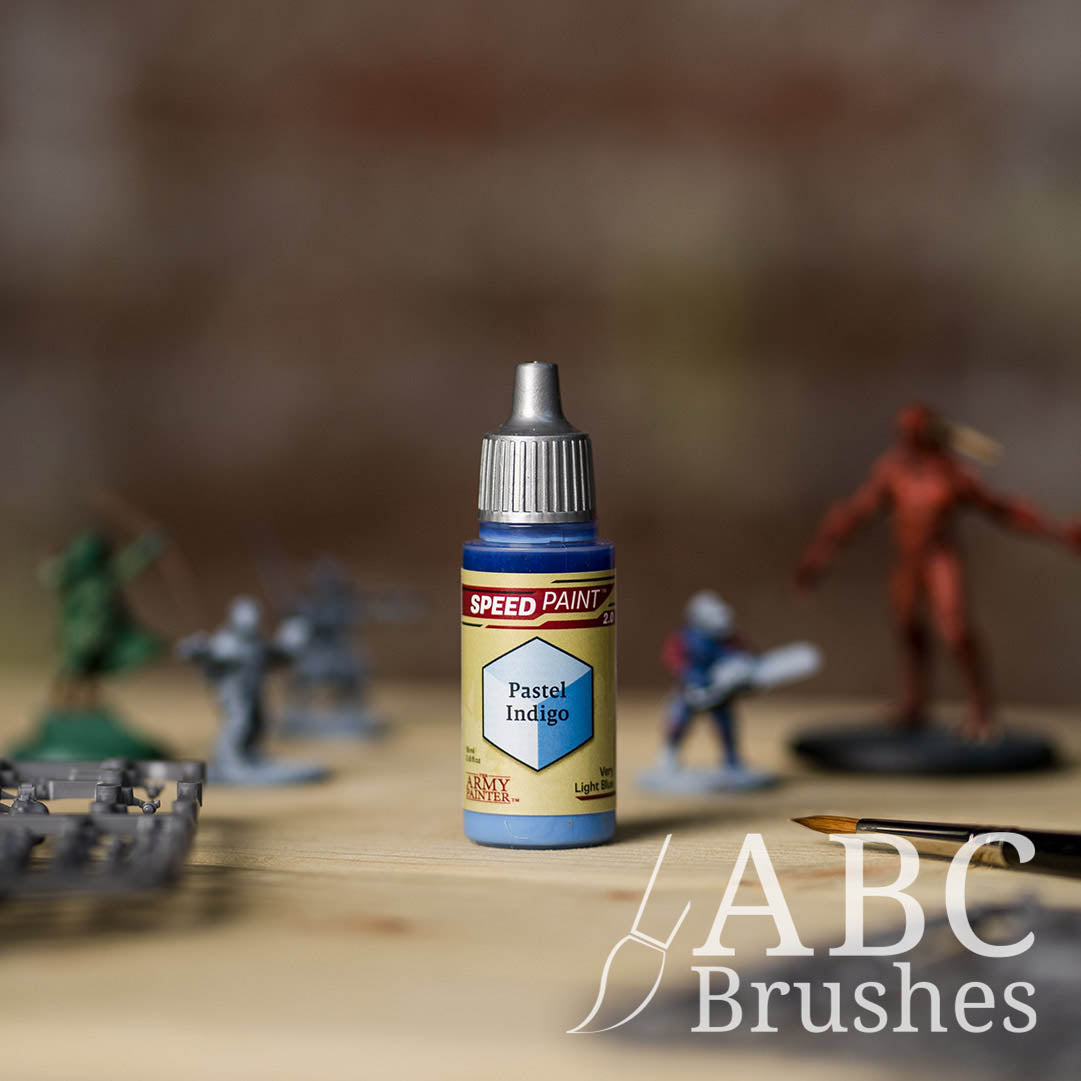 Bottle of the Army Painters Speedpaint in the colour Pastel Indigo, with wargaming models and an abc paintbrush in the background, on a wooden surface.