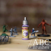 Bottle of the Army Painters Speedpaint in the colour Pastel Lavender, with wargaming models and an ABC paintbrush in the background, on a wooden surface.
