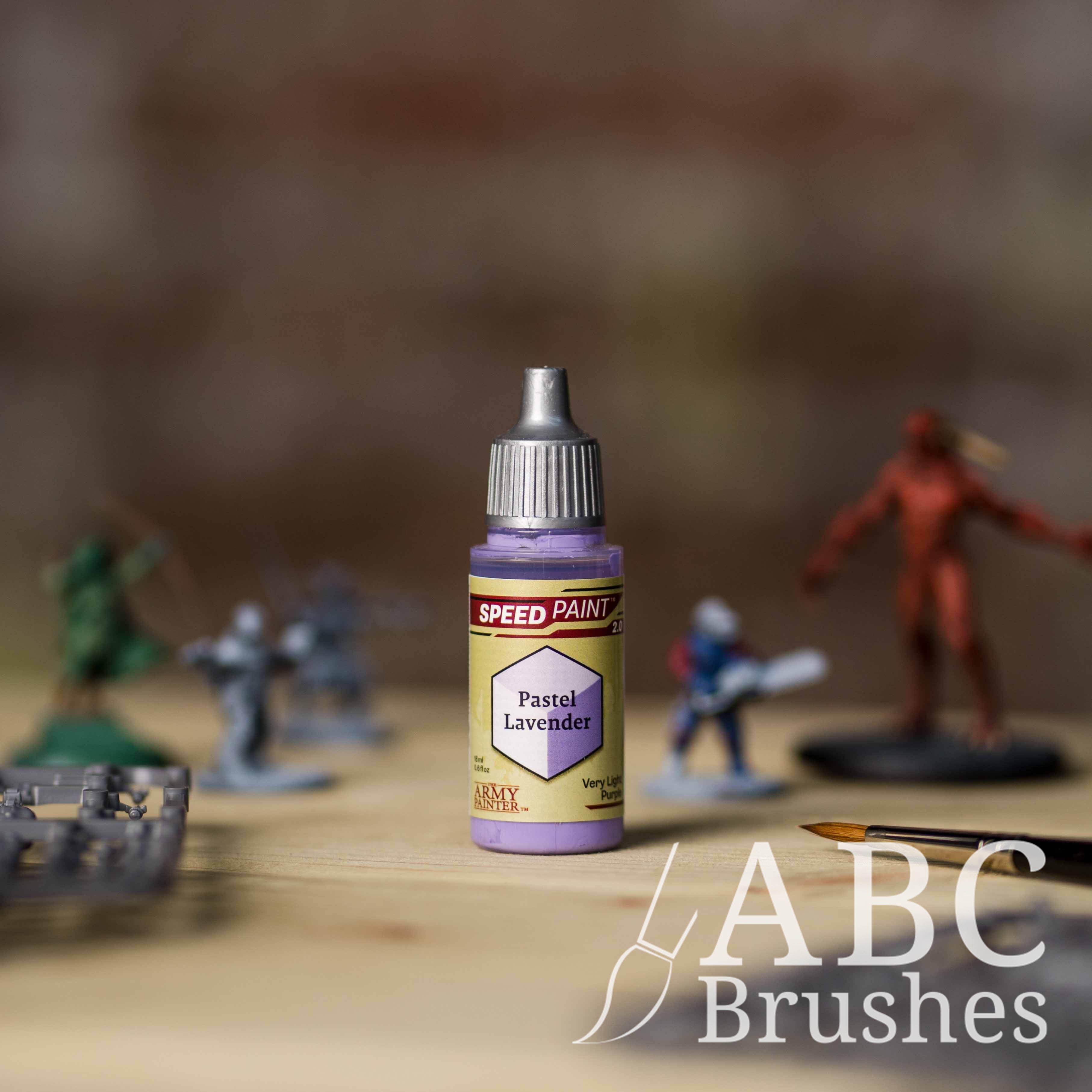 Bottle of the Army Painters Speedpaint in the colour Pastel Lavender, with wargaming models and an ABC paintbrush in the background, on a wooden surface.