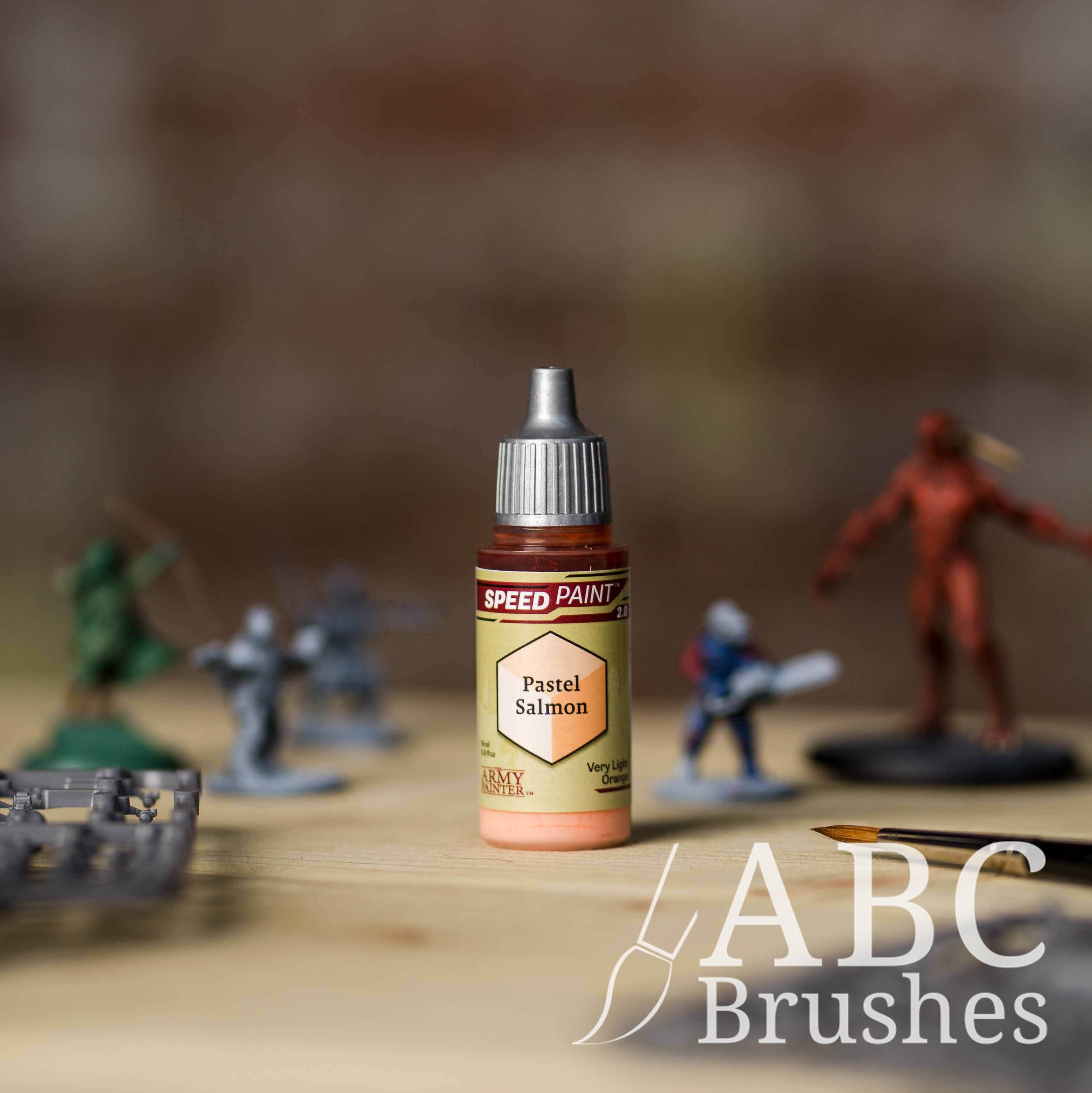 Bottle of the Army Painters Speedpaint in the colour Pastel Salmon, with wargaming models and an ABC paintbrush in the background, on a wooden surface.
