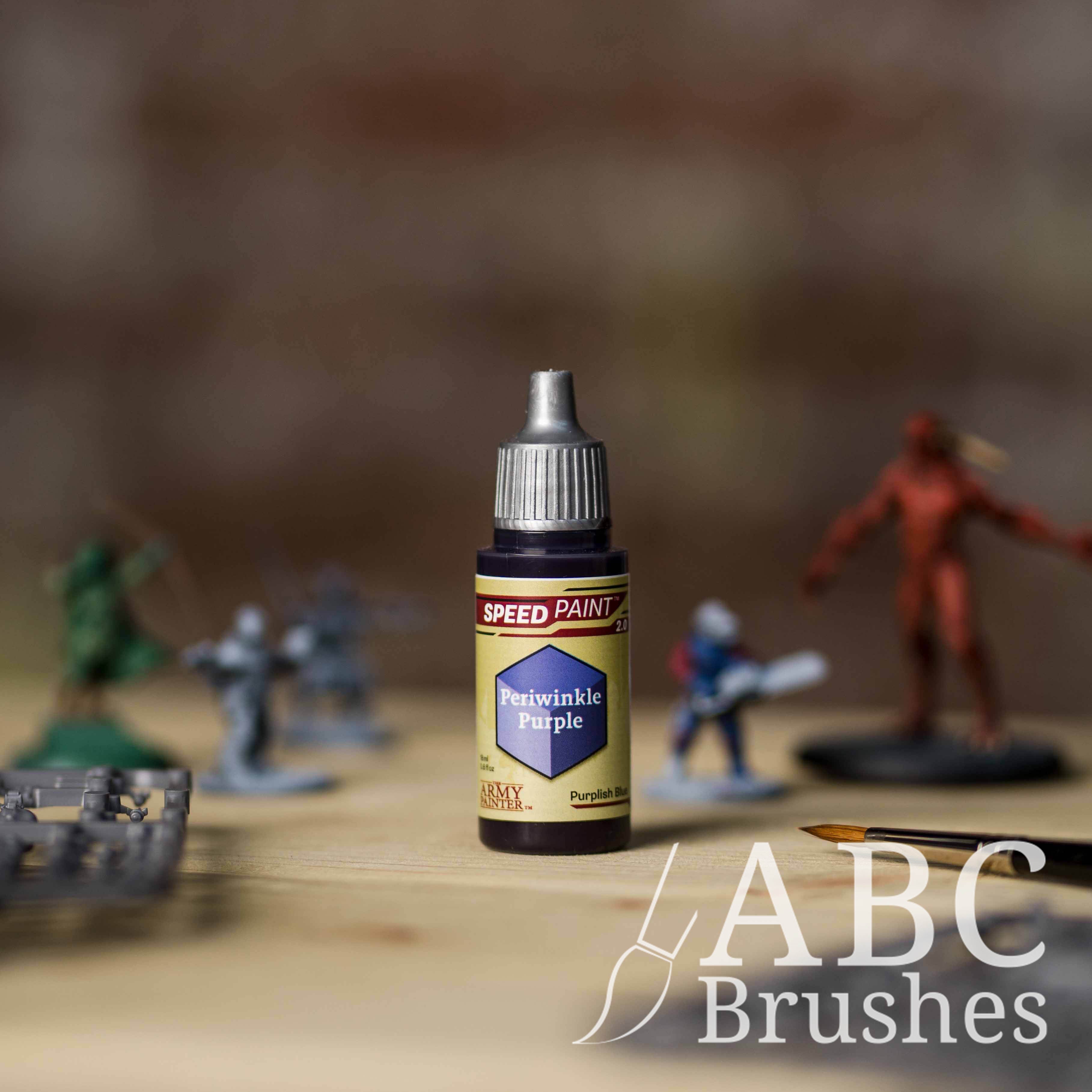 Bottle of the Army Painters Speedpaint in the colour Periwinkle Purple, with wargaming models and an ABC paintbrush in the background, on a wooden surface.