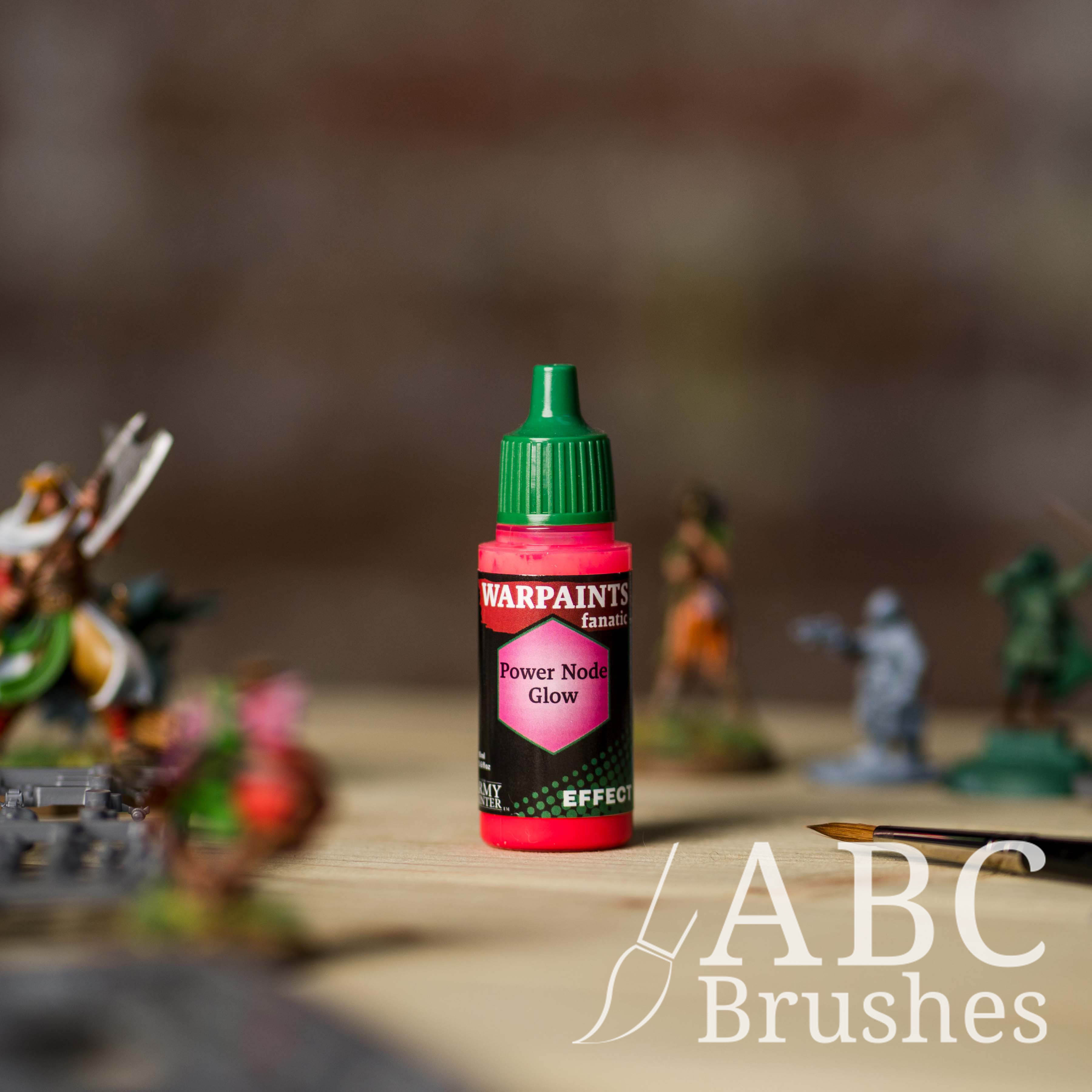 Bottle of the Army Painter Fanatics Effects in the colour Power Node Glow with various wargaming models and an ABC paintbrush in the background, on a wooden surface.