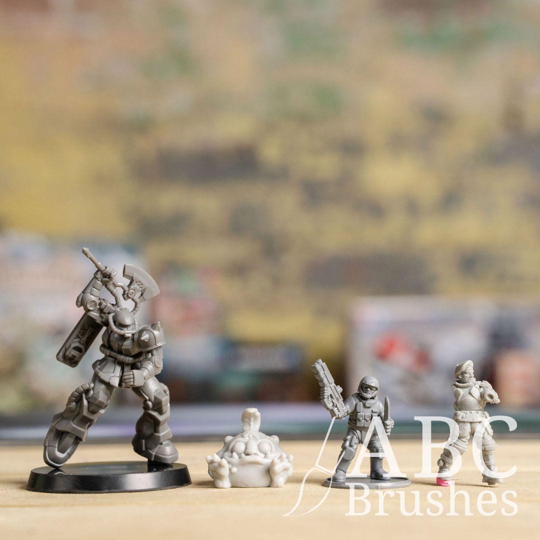 Three un-primed wargaming minis, arranged in a line on a wooden surface.
