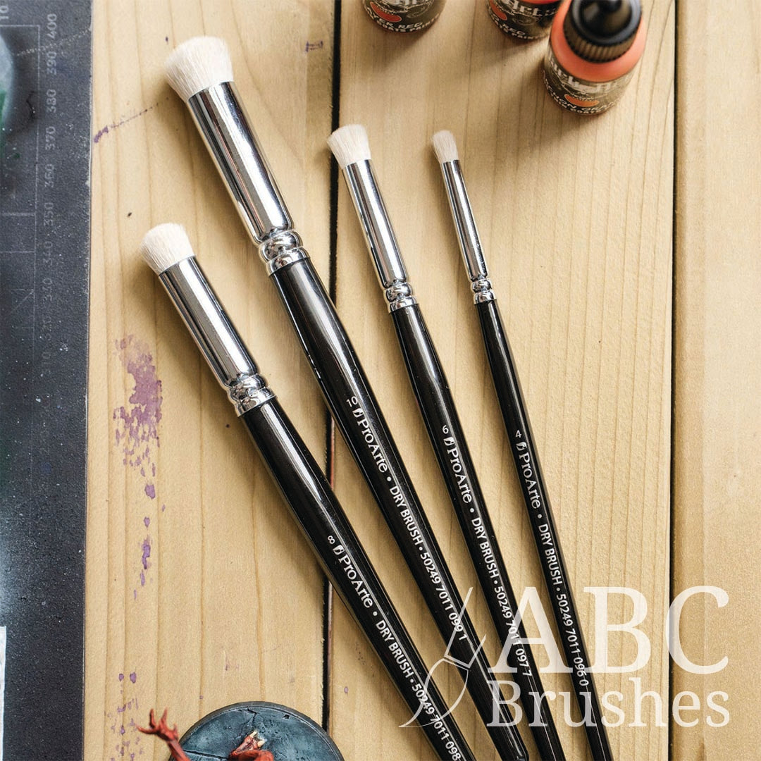 Four different sizes of Pro Arte rounded dry brushes, next to a red demon mini and three acrylic paint bottles. 