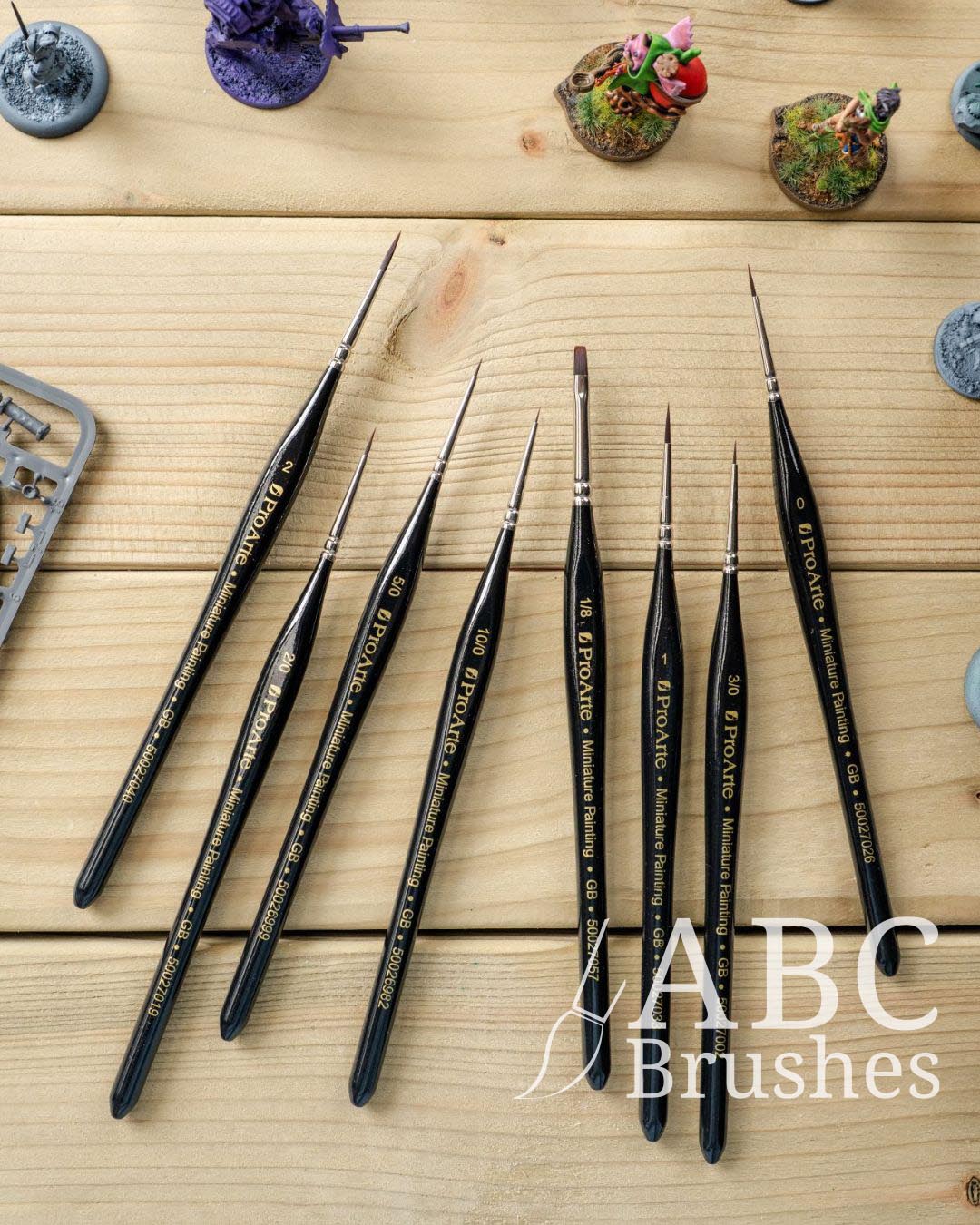 Set of Pro Miniature painting brushes against a wooden background, with a range of different minis next to them.