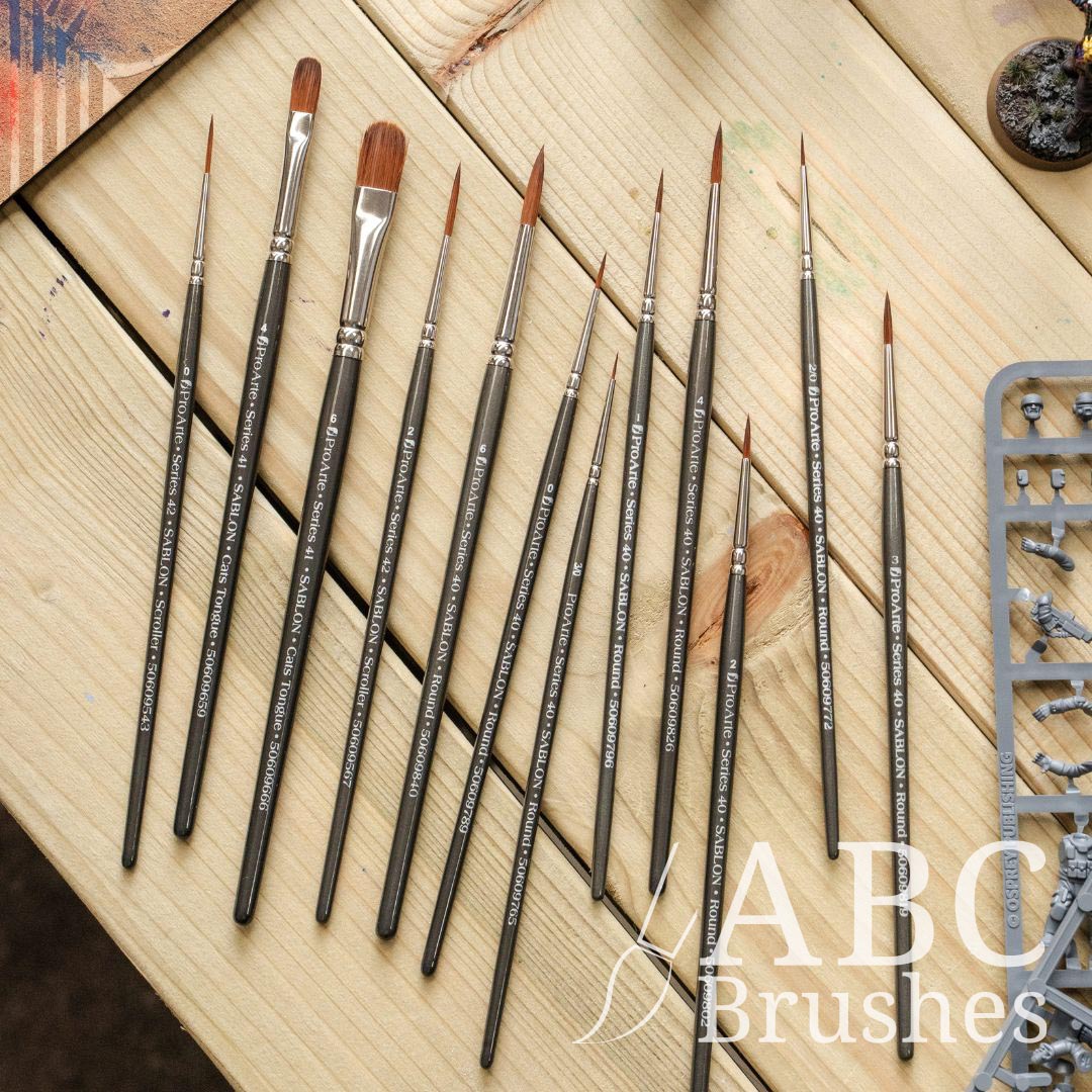 Set of Pro Arte Prolon Miniature paintbrushes against a wooden background, with a range of minis and a used dry brush board next to them.