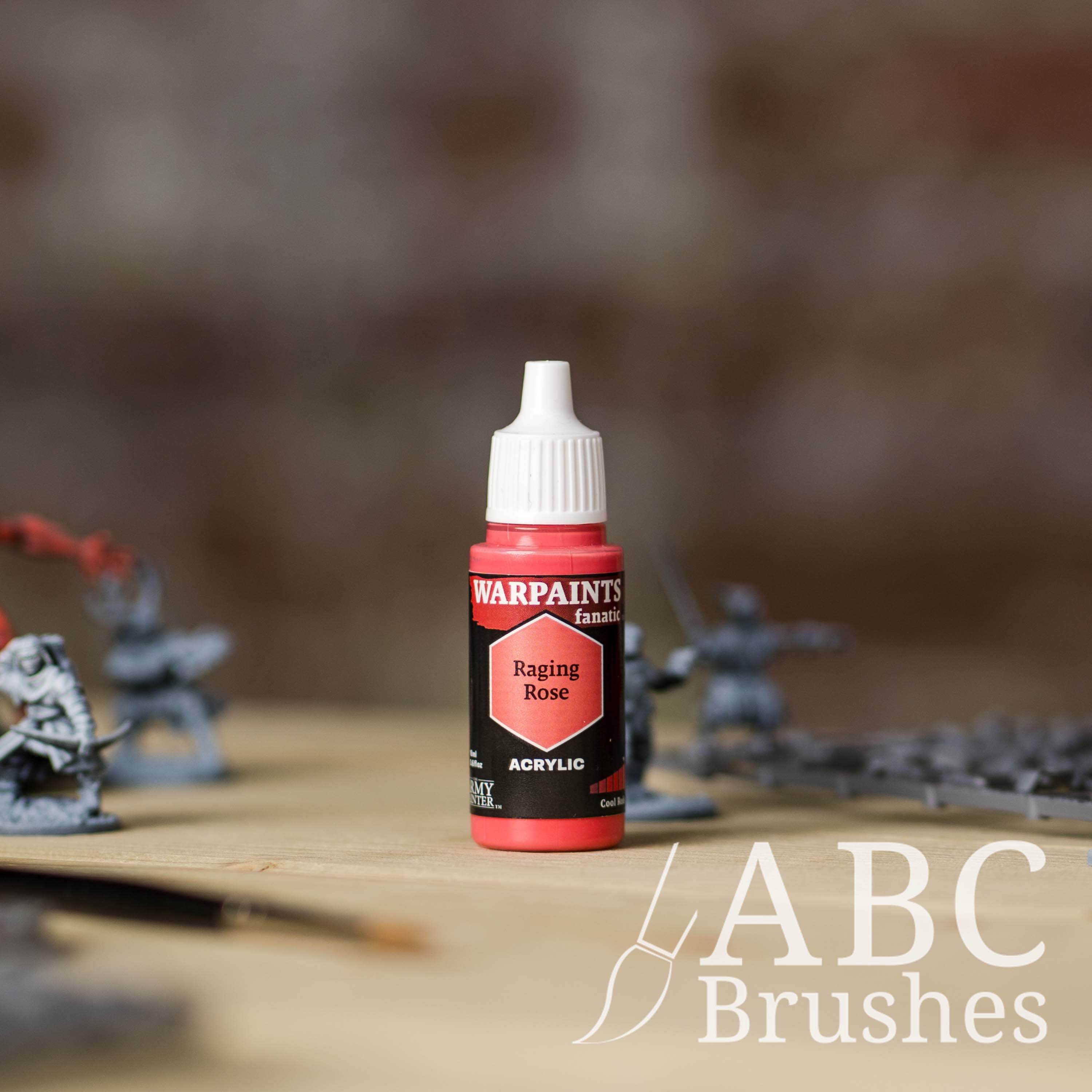 Bottle of the Army Painter Fanatics in the colour Raging Rose with various wargaming models and an ABC paintbrush in the background, on a wooden surface.