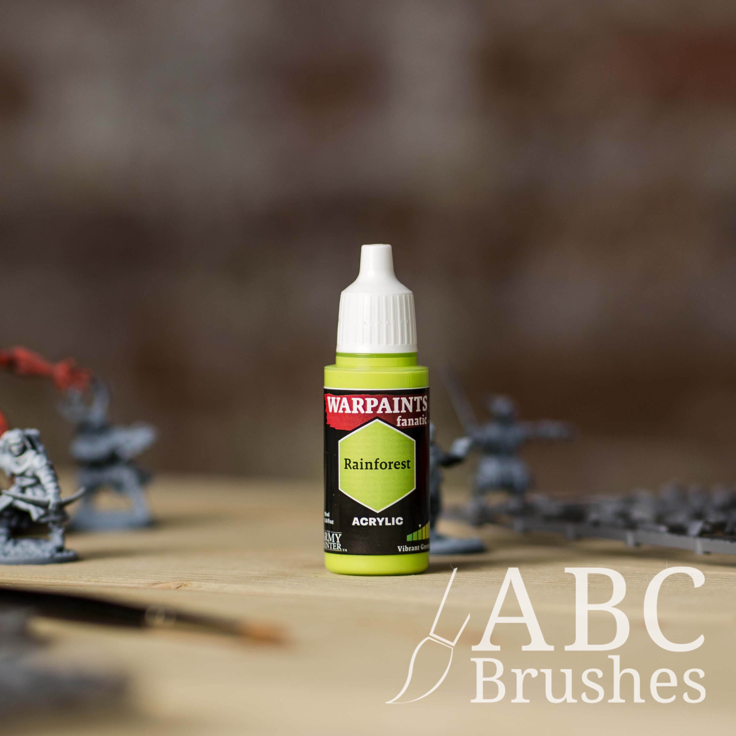 Bottle of the Army Painter Fanatics in the colour Rainforest with various wargaming models and an ABC paintbrush in the background, on a wooden surface.