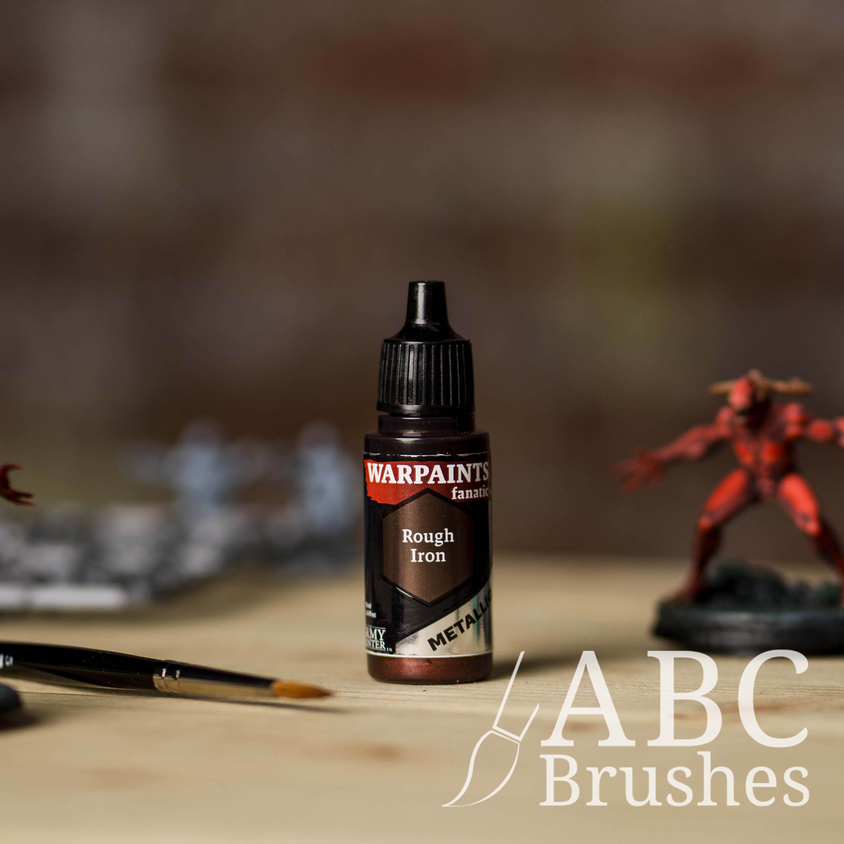 Bottle of the Army Painter Fanatics Metallic paint in the colour Rough Iron with various wargaming models and an ABC paintbrush in the background, on a wooden surface.