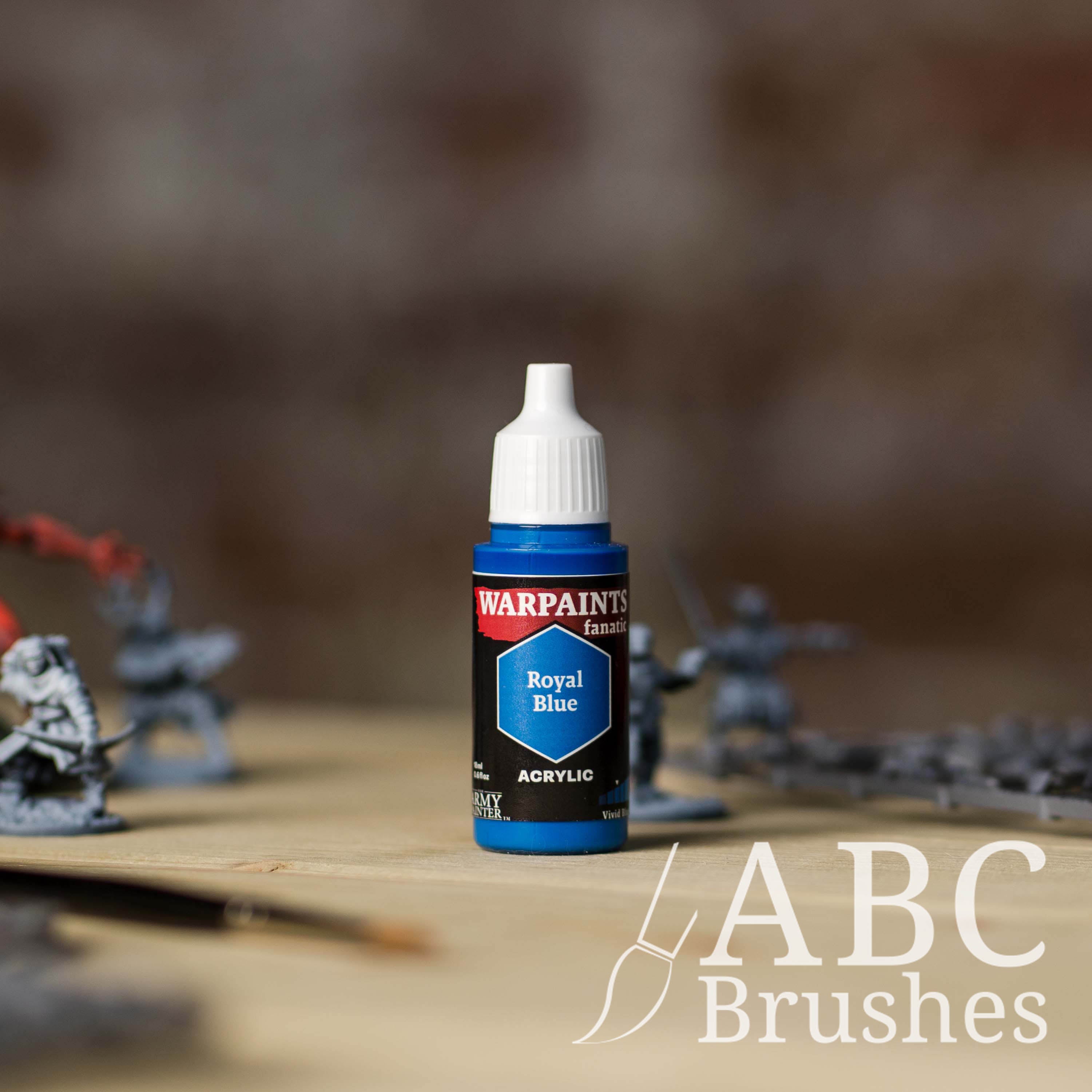 Bottle of the Army Painter Fanatics in the colour Royal Blue with various wargaming models and an ABC paintbrush in the background, on a wooden surface.
