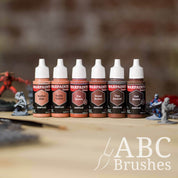 Army Painter Fanatics Ruddy Browns Triad on a wooden surface. There are wargaming models and an ABC paint brush next to them.