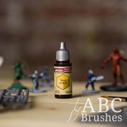 Bottle of the Army Painters Speedpaint in the colour Sand Golem, with wargaming models and an ABC paintbrush in the background, on a wooden surface.
