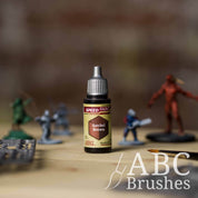Bottle of the Army Painters Speedpaint in the colour Satchel Brown, with wargaming models and an ABC paintbrush in the background, on a wooden surface.