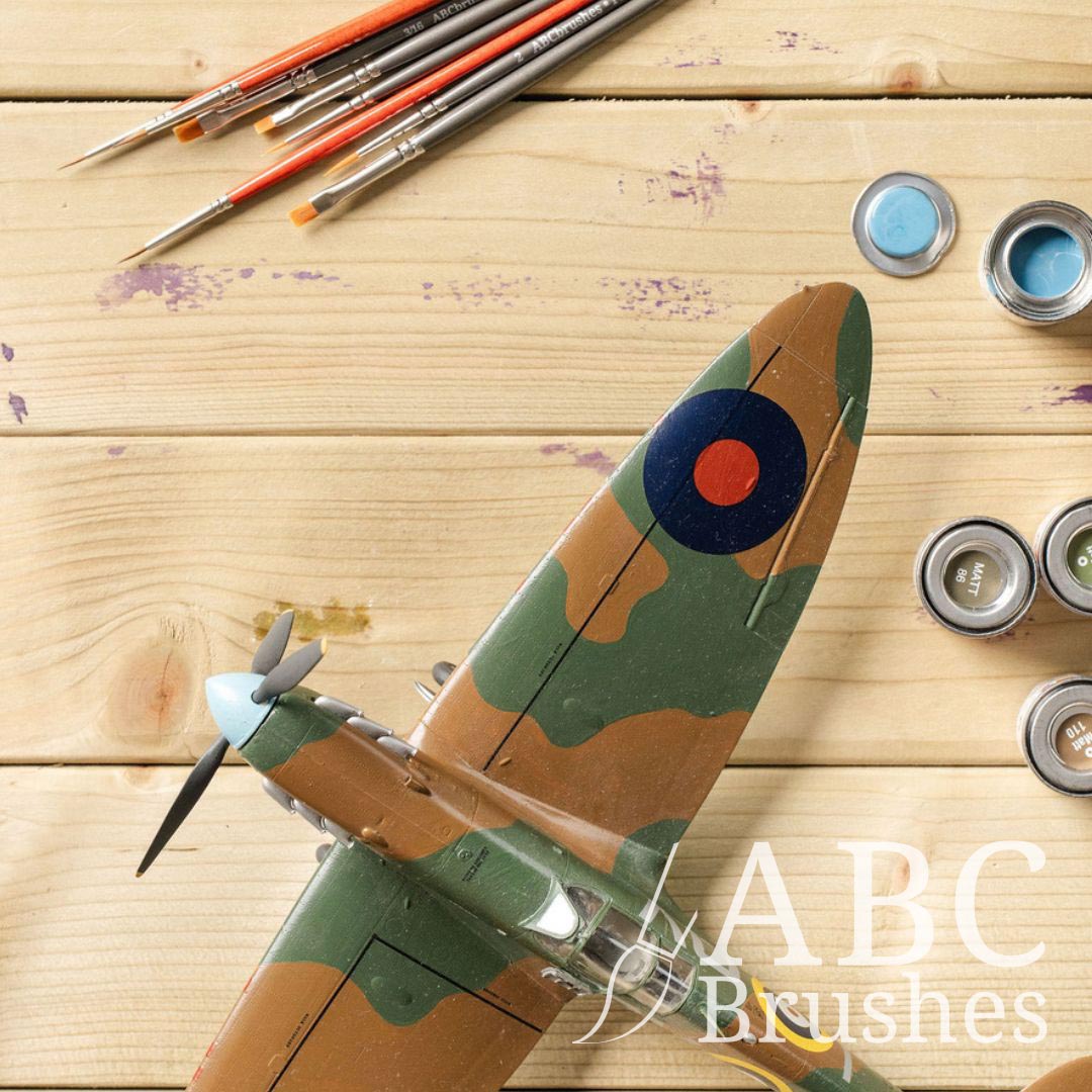 Top view of a scale model aeroplane with enamel paint pots and paintbrushes next to it. 
