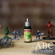 Bottle of the Army Painters Speedpaint in the colour Shamrock Green, with wargaming models and an ABC paintbrush in the background, on a wooden surface.