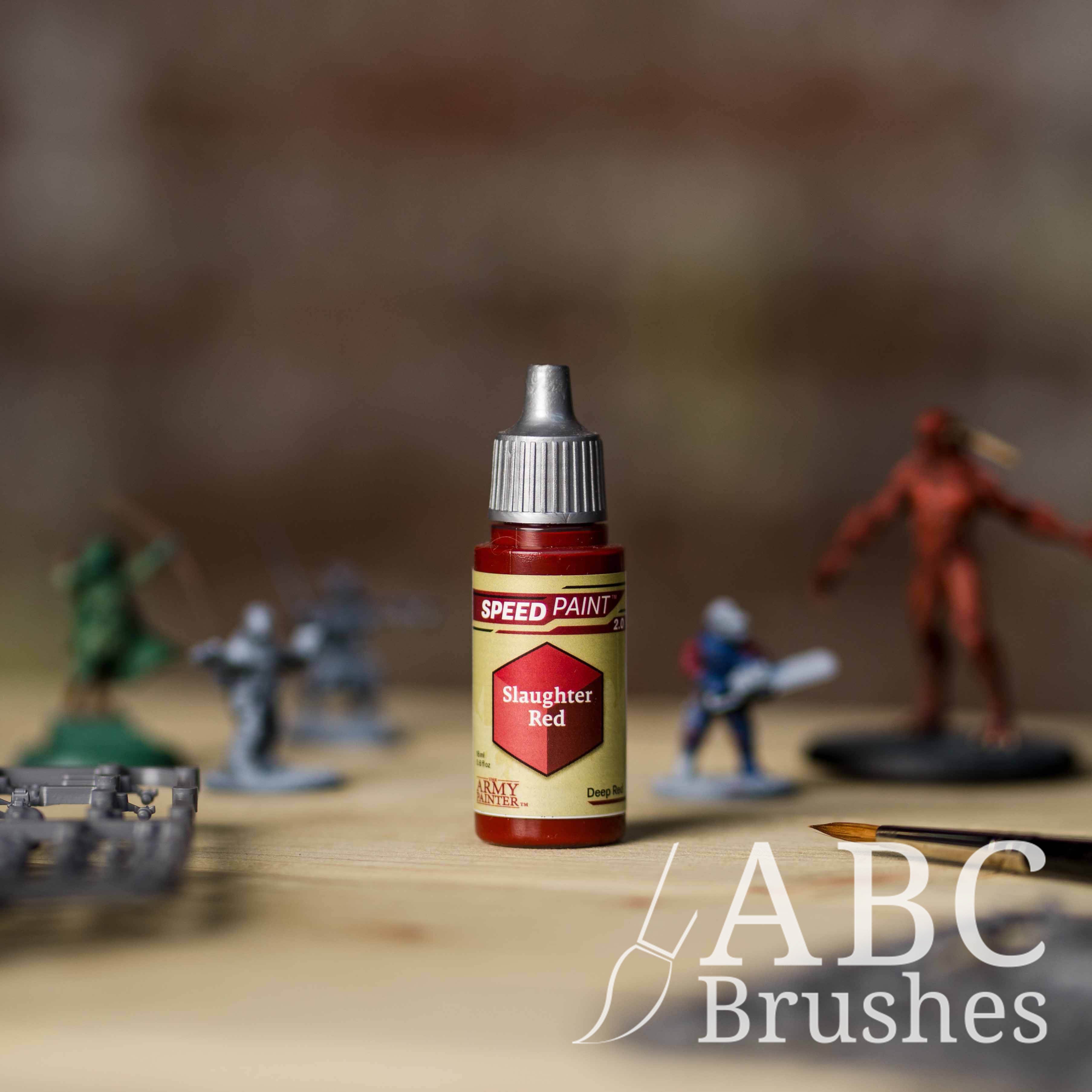 Bottle of the Army Painters Speedpaint in the colour Slaughter Red, with wargaming models and an ABC paintbrush in the background, on a wooden surface.
